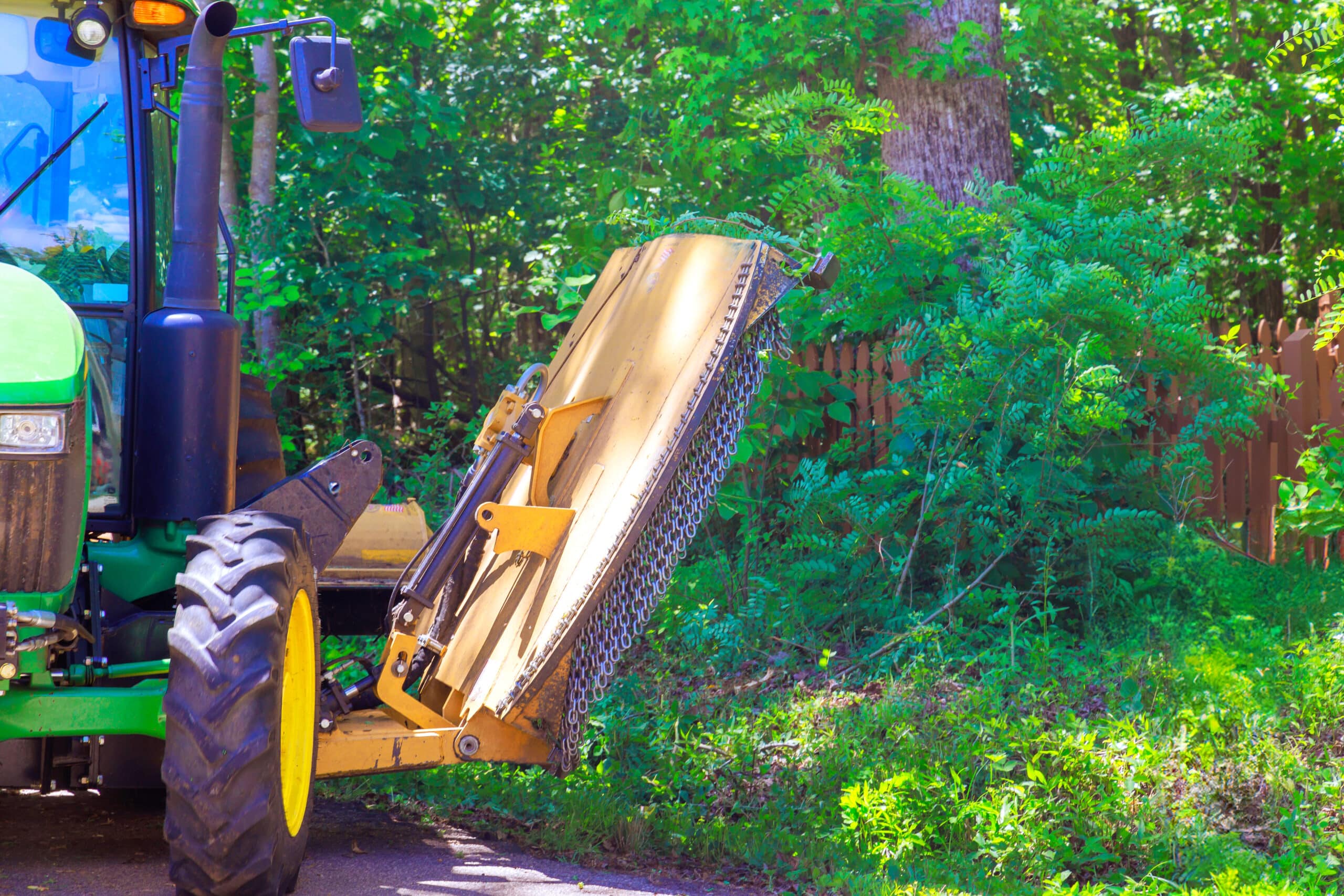 Municipal service tractor with mower cutting grass branches on both sides of road